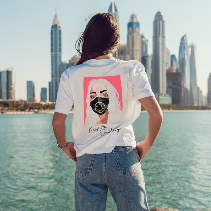 Juxar white graphic print boyfriend tee featuring colorful masked woman design on back by waterfront skyline