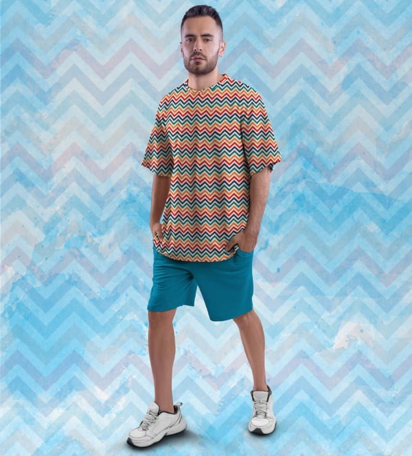 Male model wearing Juxar oversized printed t shirt with graphics multicolor chevron pattern teal shorts and white sneakers