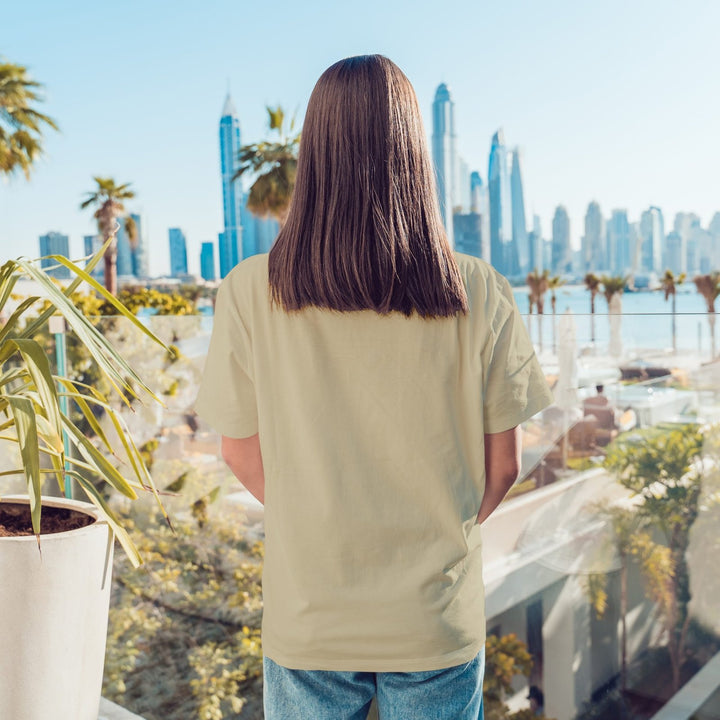 Juxar boyfriend fit printed t shirt back view on model wearing beige tee and jeans overlooking city skyline