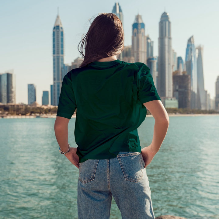 Juxar designer boyfriend t shirt dark green on woman back view with jeans by city skyline waterfront