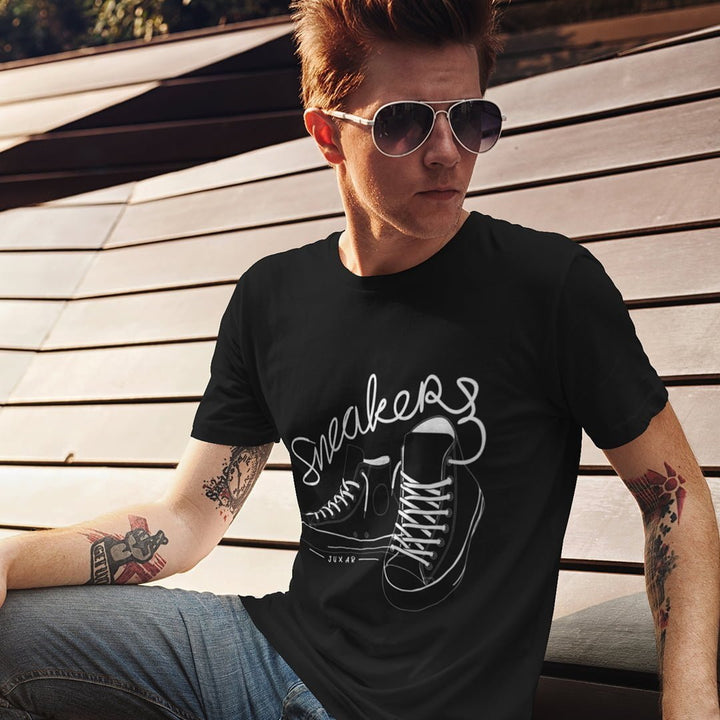 Juxar sneaker graphic t-shirt in black worn by a man sitting outdoors with sunglasses and tattoos
