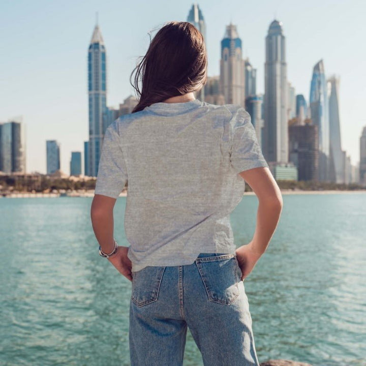 Juxar graphic boyfriend t shirt back view on model by waterfront with city skyline wearing light gray tee and relaxed jeans