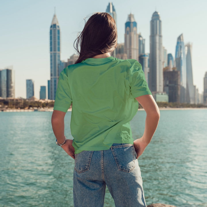 Juxar summer boyfriend t shirt in green worn by model with jeans facing waterfront city skyline
